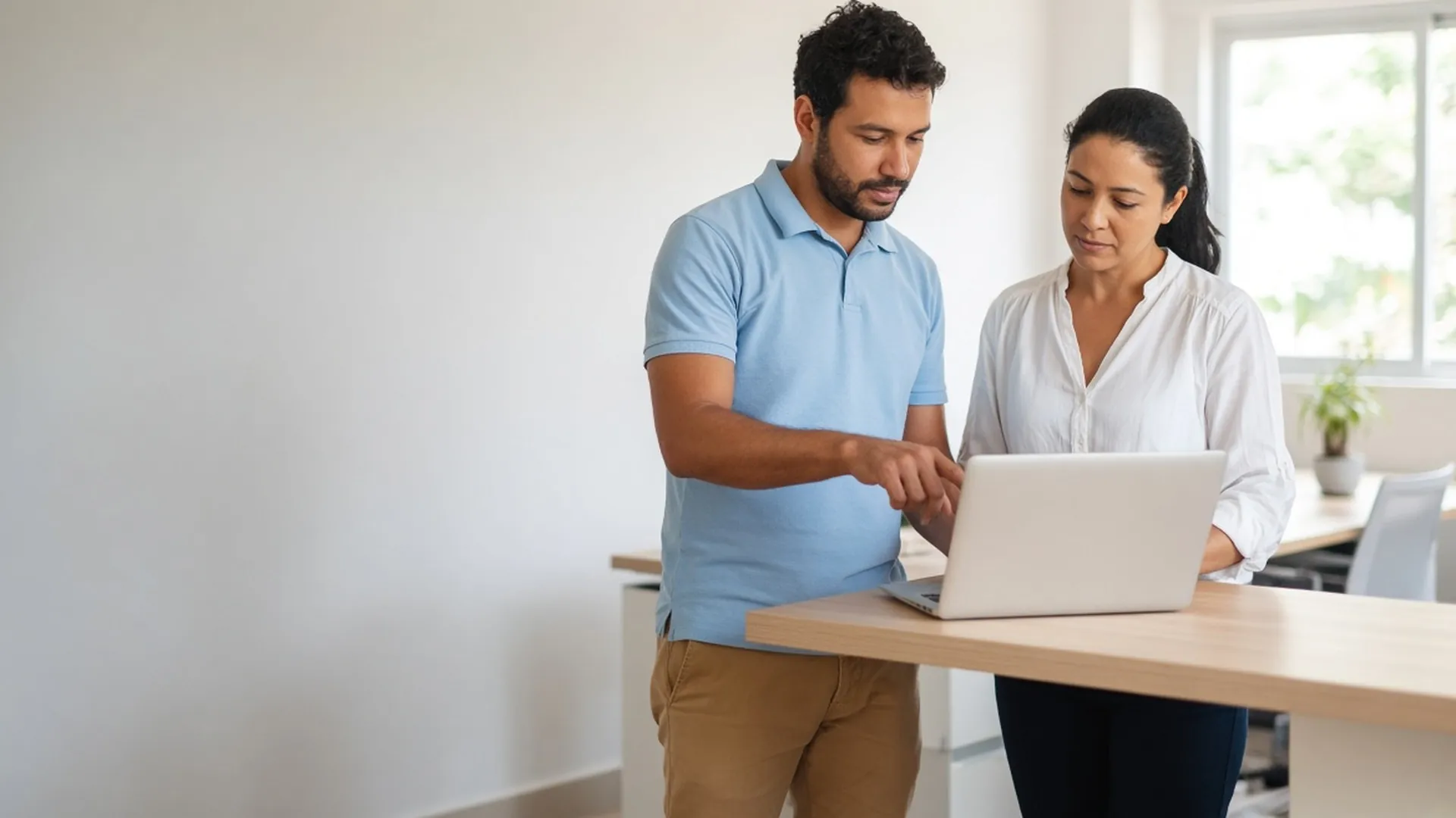 Técnico de TI orientando uma pessoa em frente ao notebook, em escritório claro